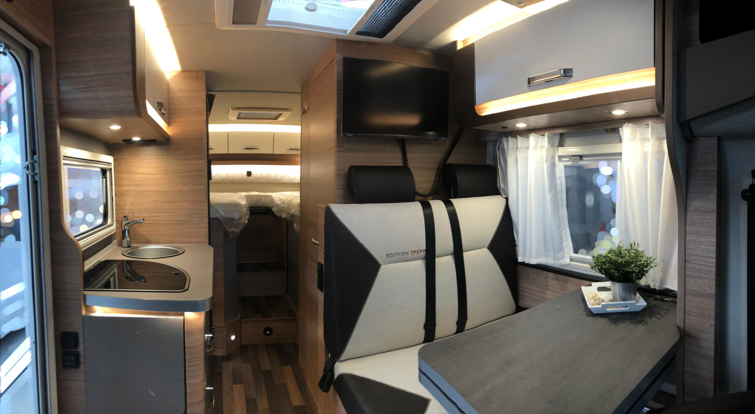 Innenansicht des Wohnmobils vom Fahrerhaus aus mit Blickauf komplette Sitzecke, Küche und Bett